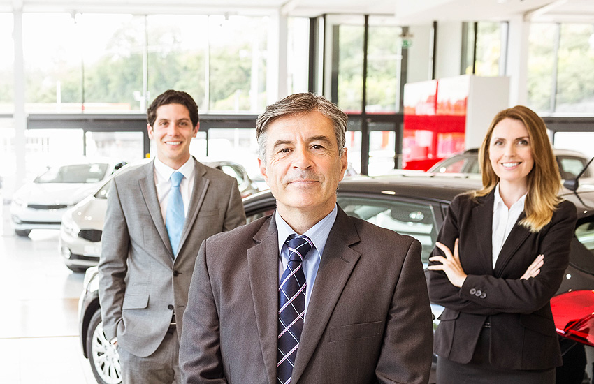A GMC sales team stands ready and smiling to greet new customers in the bright and sunny showroom