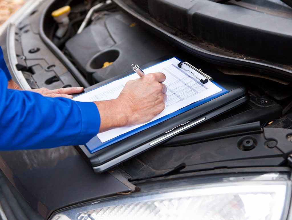 Summer Road Trip Maintenance Professional checks off tasks as he prepares an SUV engine for a road trip