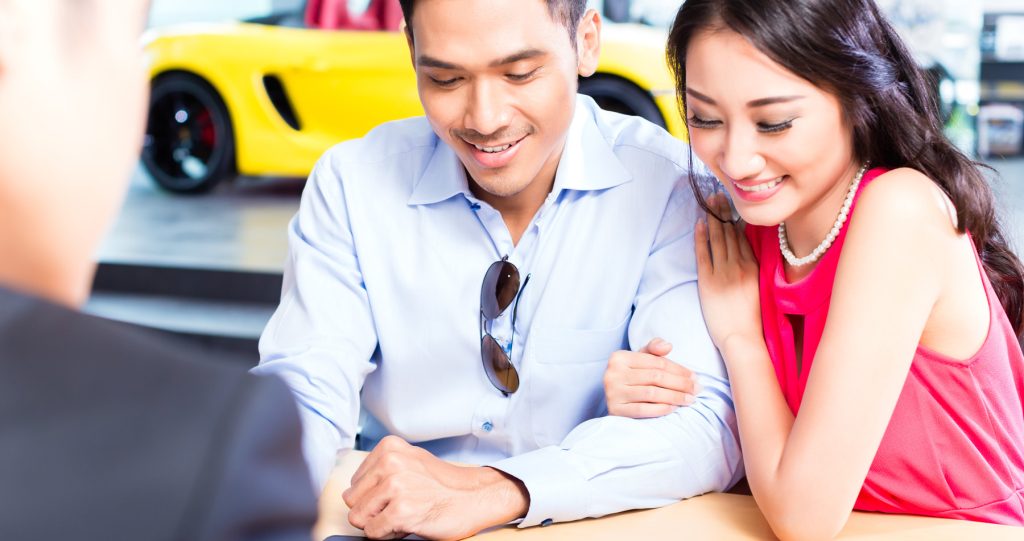 A smiling young couple are in a GMC Car showroom being shown the Financing Plan by a representative.